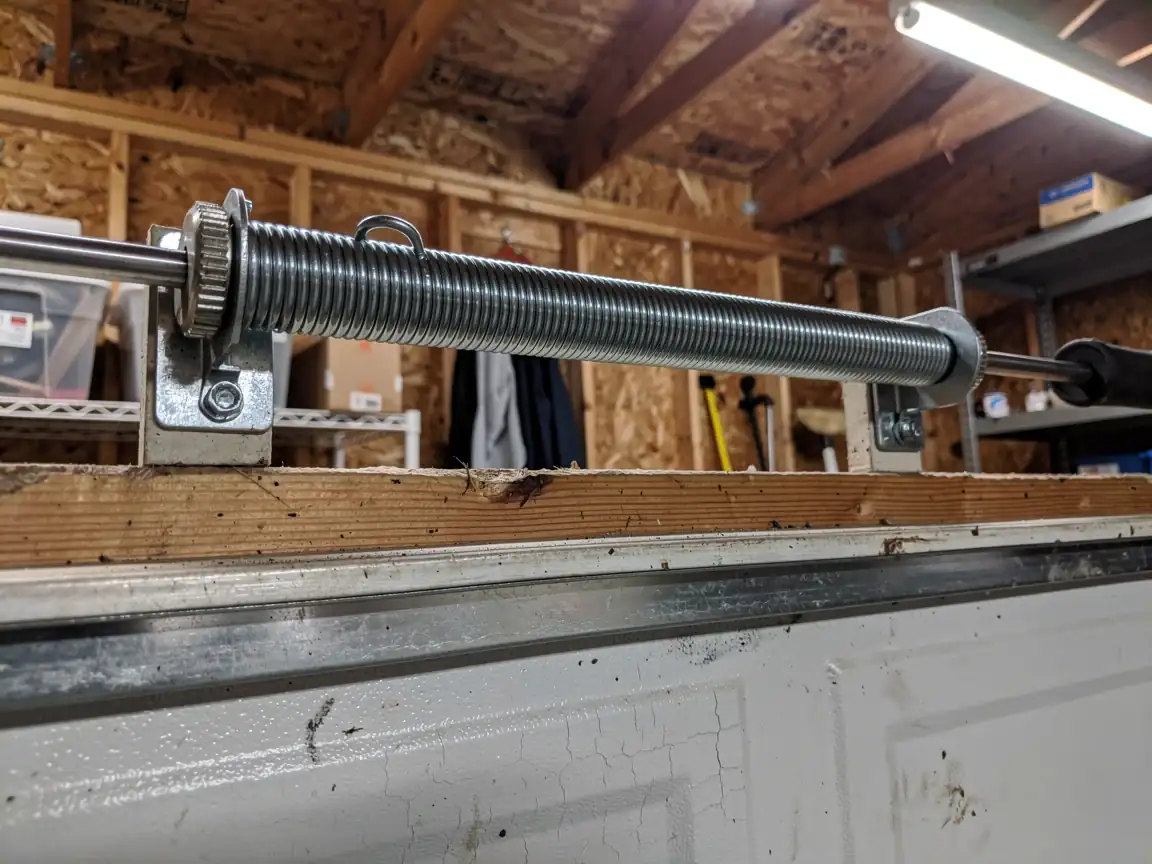 A garage door torsion spring is mounted above a white garage door.